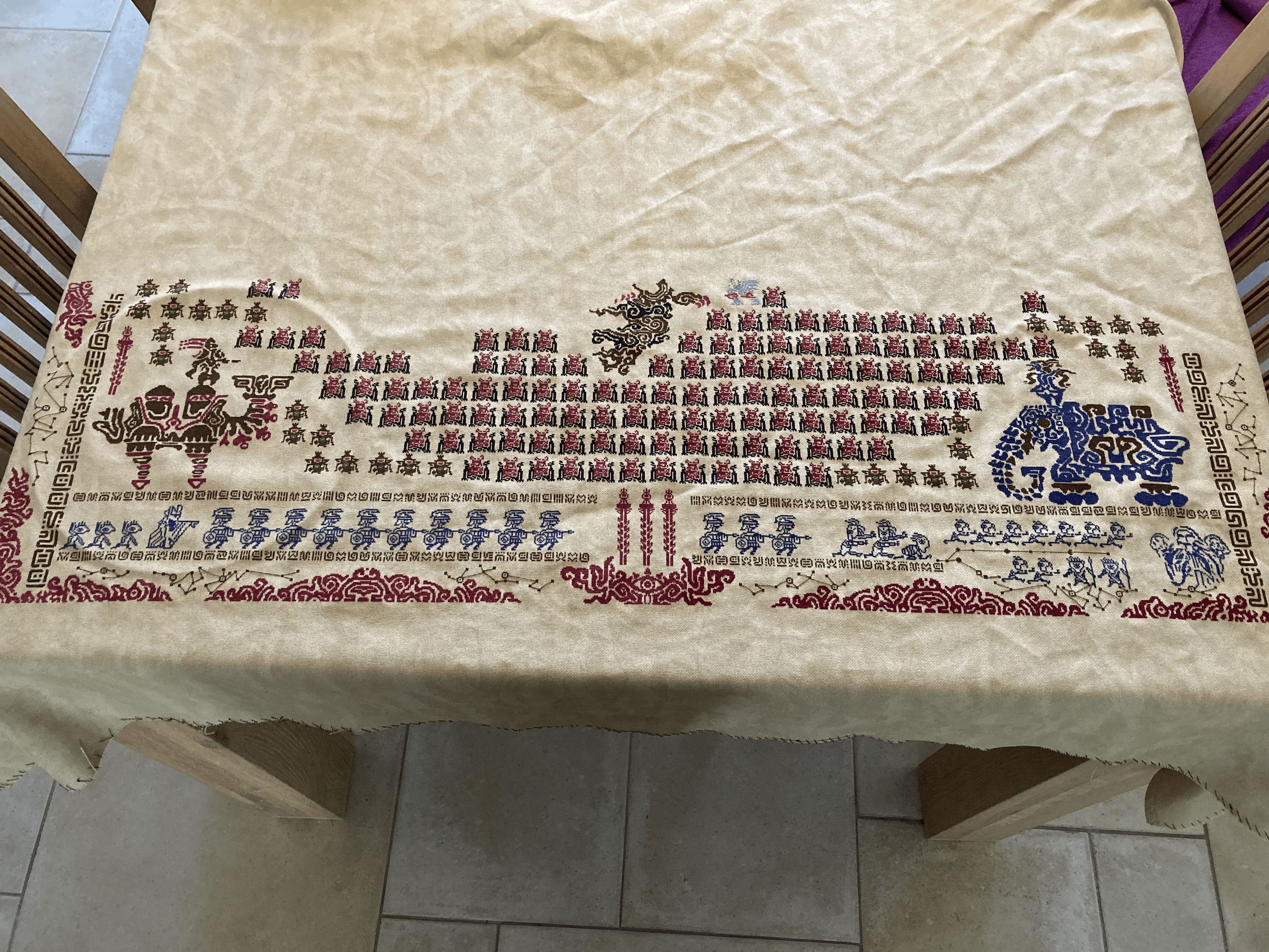 A large piece of fabric laid out over a table. Half of an elaborate pattern is stitched onto it